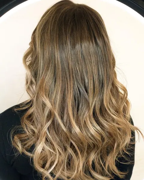 Balayage avellana con reflejos dorados miel sobre pelo ondulado, visto de espaldas
