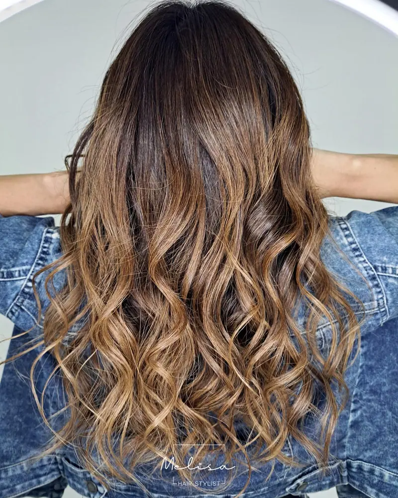 Balayage brondé en tonos avellana y beige sobre pelo ondulado, visto de espaldas